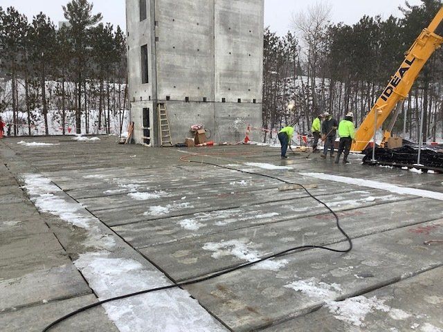 Workers near concrete tower being built outdoors with a crane. Snow covers the ground.