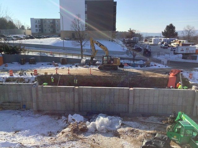 Construction site with excavator and workers, dirt, concrete walls, snow. Sunny day.