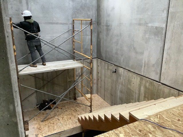 Person on scaffolding in a concrete room, constructing a structure with stairs.