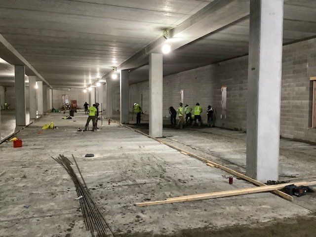 Construction site interior: workers in safety vests, concrete pillars, and exposed rebar.