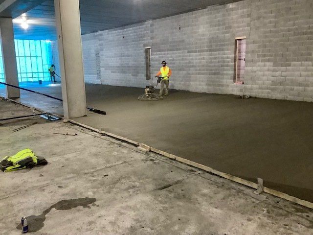 Construction worker smoothing wet concrete floor with machine, inside building.