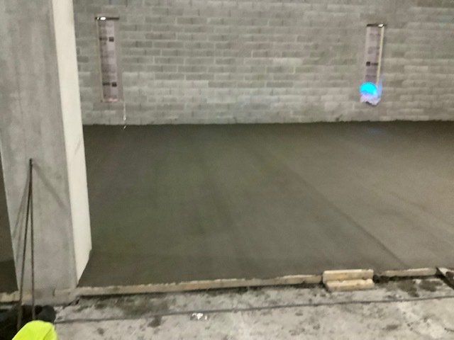 Freshly poured concrete floor in an unfinished room with brick and concrete walls. Level markers are visible.