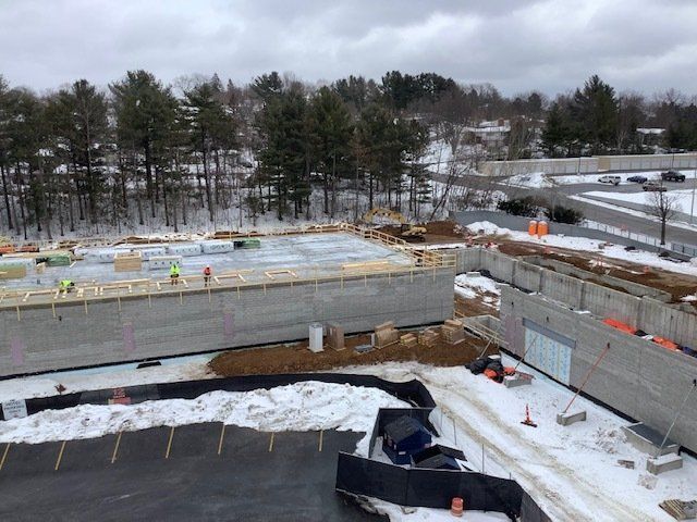Construction site in winter with concrete walls, some workers, and snow-covered ground.