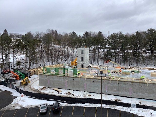 Construction site with concrete foundation, tower, and workers; snowy landscape in background.