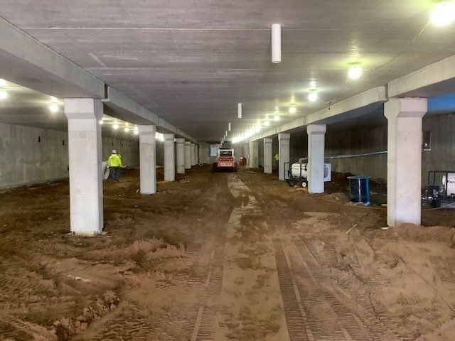 Underground construction site with dirt floor, pillars, and a small vehicle. A worker in a vest is visible.