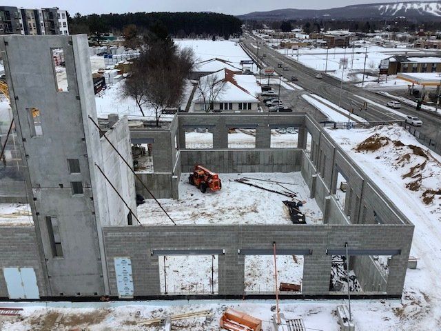Construction site: concrete building walls, orange lift, snow-covered ground, road in background.