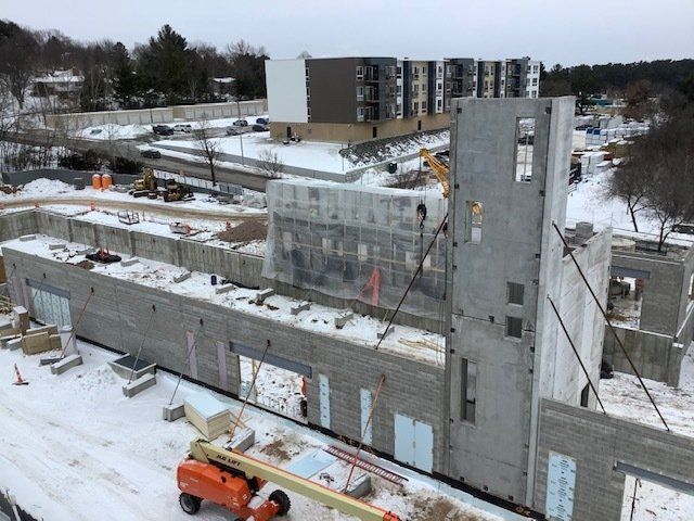 Construction site with concrete walls being erected, snowy ground. Crane lifting a wall panel.
