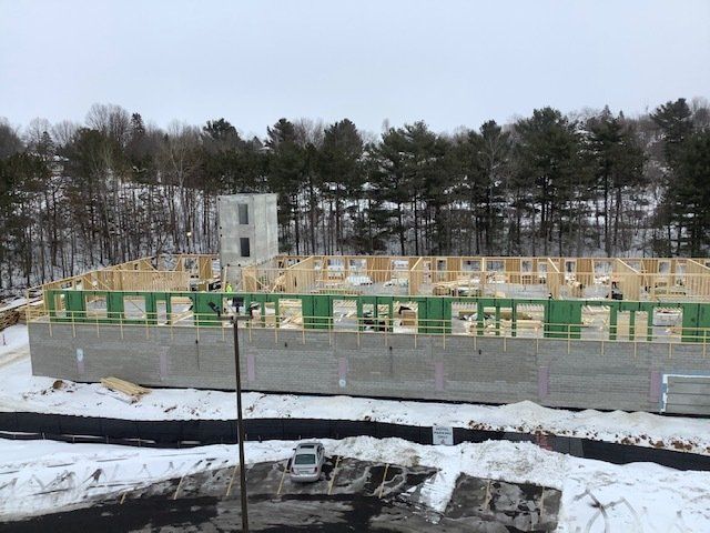 Construction site in winter; wooden framing on a concrete foundation, snowy ground, trees in the background.