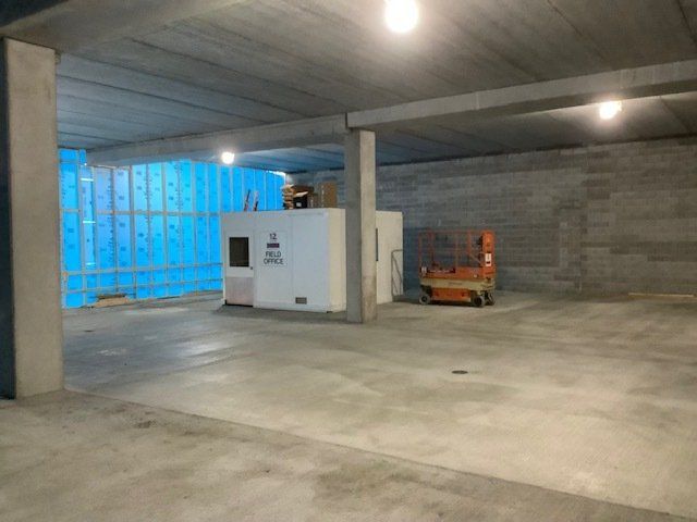 An empty concrete room under construction with a white utility box and orange lift.