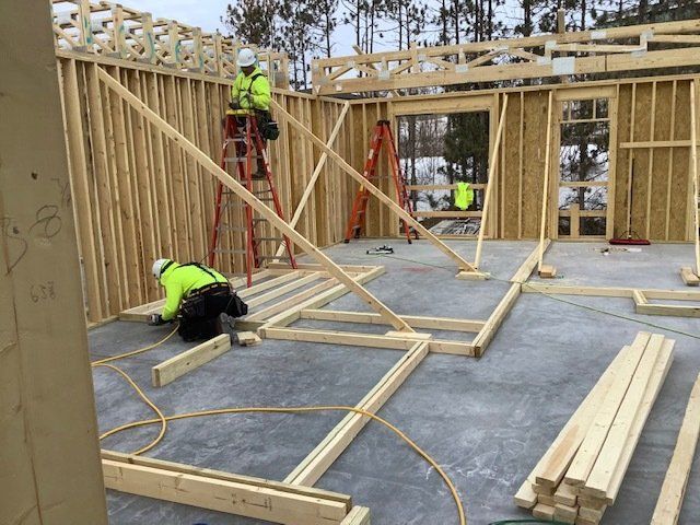 Construction workers framing a new building with lumber on a concrete floor.
