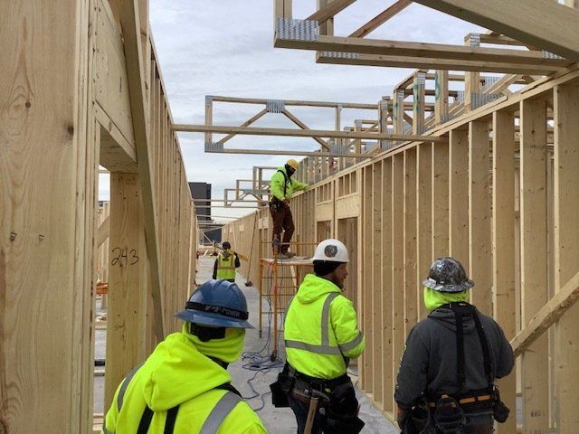 Construction workers building a wooden structure outdoors. Wearing high-visibility vests and hard hats, they are on scaffolding.