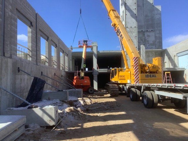 Construction site with a crane lifting a concrete beam; orange lift.