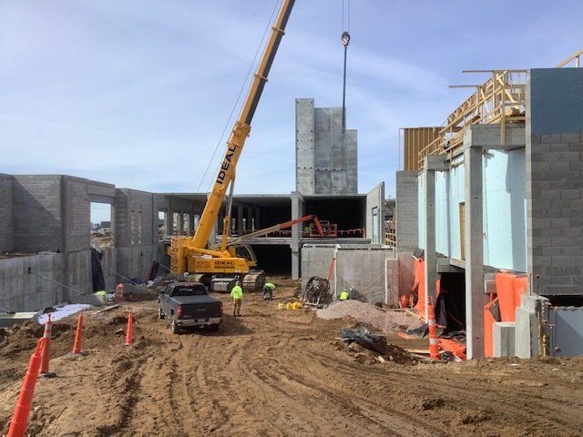 Construction site with a large yellow crane lifting a concrete wall. Workers and vehicles present.
