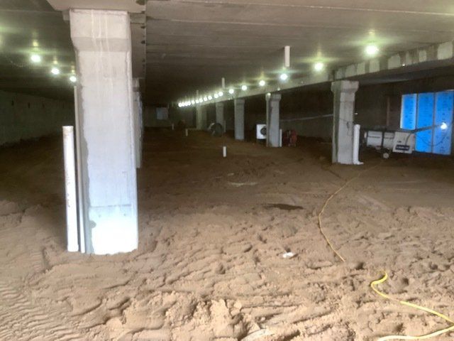 Underground area with concrete pillars, dirt floor, and overhead lighting. Construction in progress.