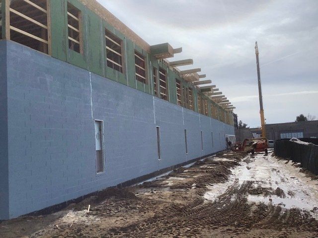 Building under construction; exterior view shows blue-painted concrete block wall and wooden framework above; cloudy sky.