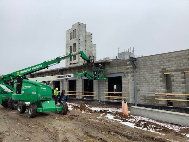 Construction site with green boom lifts and workers on a partially built stone building.