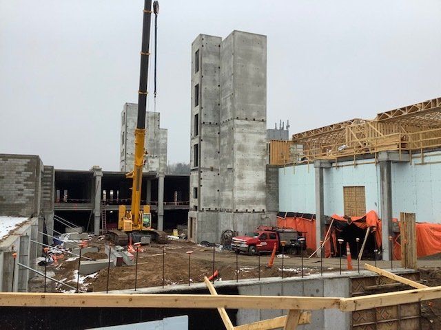 Construction site with crane, concrete structures, and exposed wooden framing. Cloudy day.