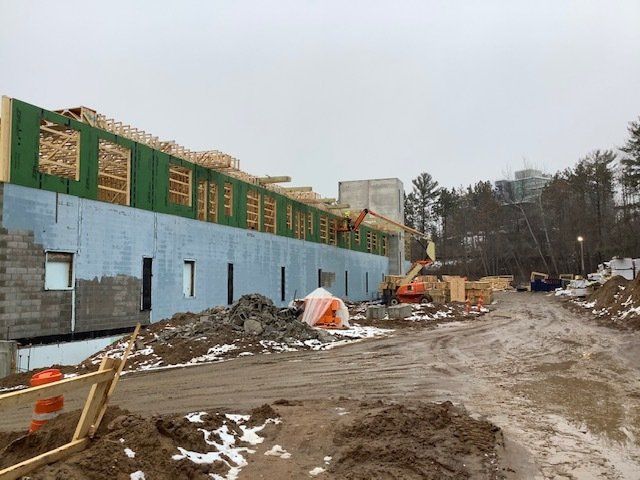 Construction site; blue-walled building under construction; muddy ground with equipment and overcast sky.