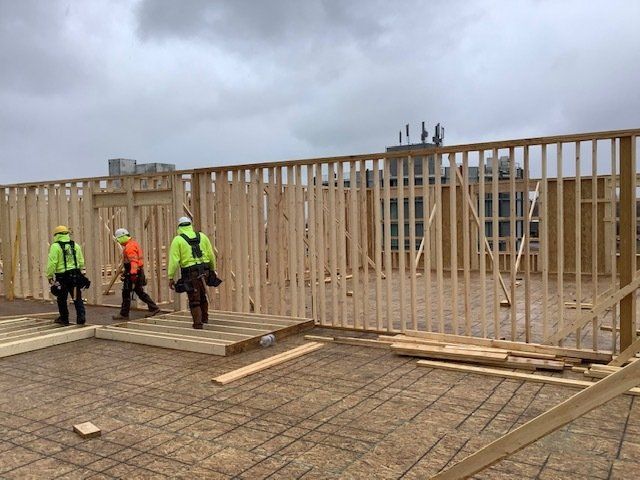 Construction workers framing a wall on a concrete surface, cloudy sky overhead.