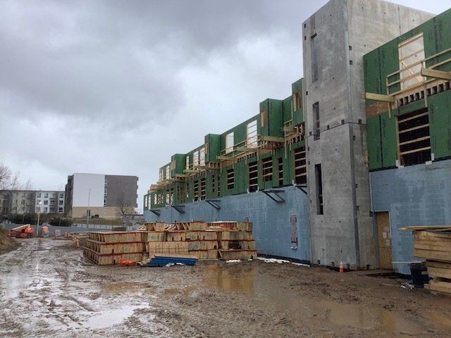Construction site with buildings under development. Muddy ground, grey sky, and materials visible.