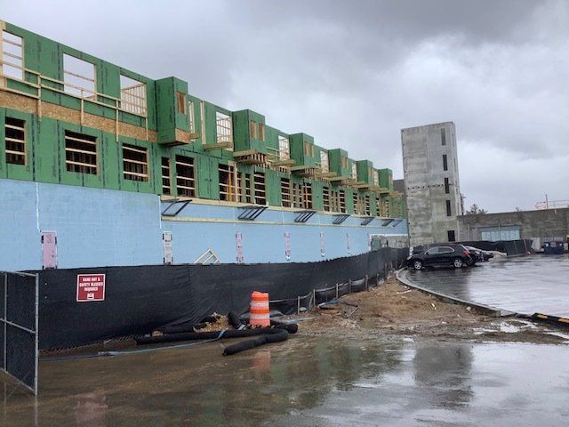 Construction site with partially built buildings. Green framing, blue insulation, and a tower are visible.