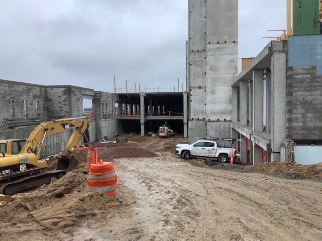 Construction site with excavator and truck; partially built concrete buildings on a cloudy day.
