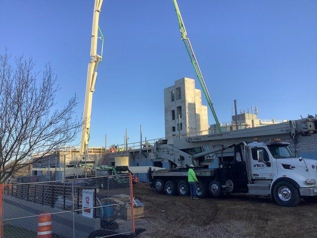 Concrete being pumped at a construction site by two crane trucks on a sunny day.