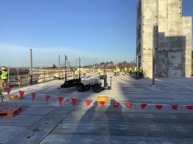 Construction workers on a concrete rooftop, setting up equipment with safety flags and a tall, unfinished building in the background.