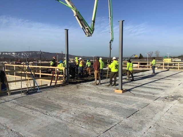 Construction workers pouring concrete with a boom pump at a job site. Several workers wear safety vests.