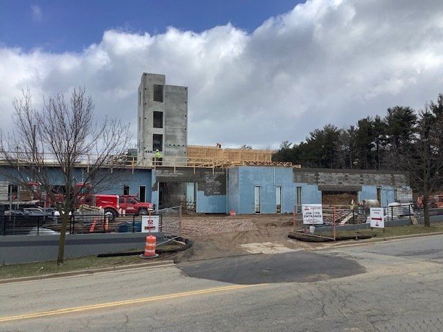 Construction site of a light blue and gray building with a tall tower under a cloudy sky.