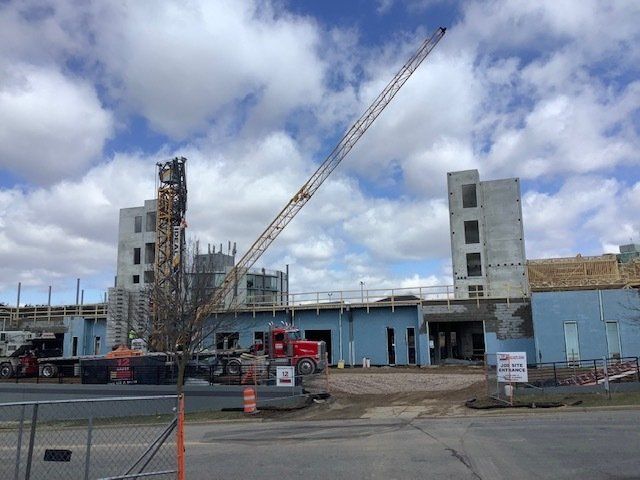 Construction site with crane, blue walls, unfinished buildings, under cloudy sky.