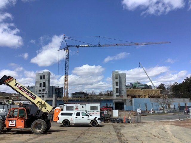Construction site with a crane and telehandler under a partly cloudy sky.