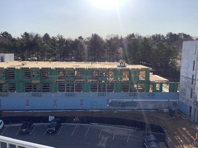 Building under construction, wood frame structure, workers on roof, blue panels, sunny day.