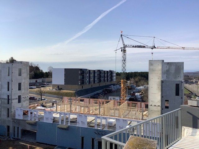 Construction site with crane, partially built structures, and a multi-unit building in the background. Blue sky.