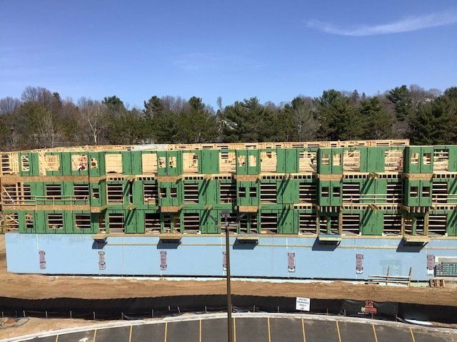 Multi-story building under construction; green wooden framing, blue base, clear sky.