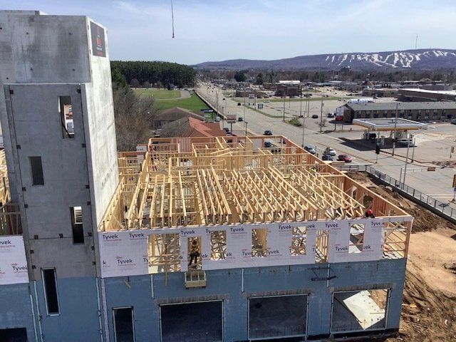 Construction site, wood framing on a building's roof with concrete walls, highway, and mountain background.