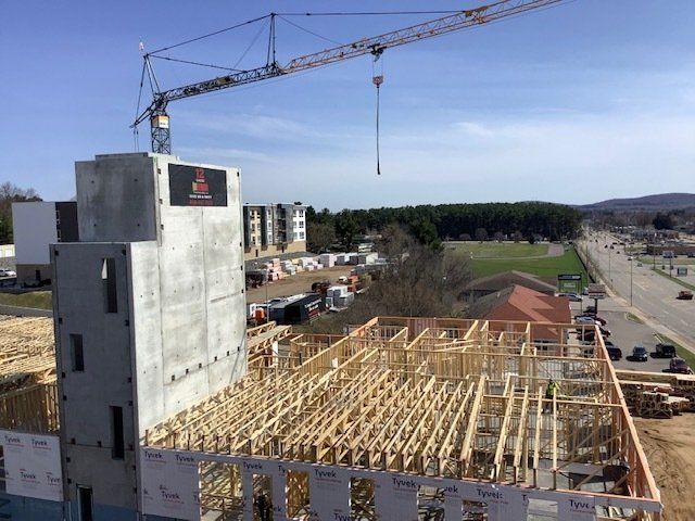 Construction site with crane, partially built building, wooden beams, concrete tower, blue sky, and roadway.