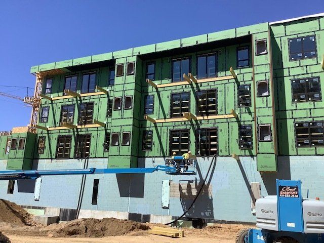 Building under construction with green siding, windows, and a blue lift.