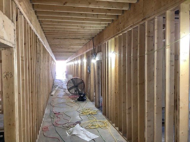 Wooden hallway under construction with framing and electrical wiring; fan and light in the distance.