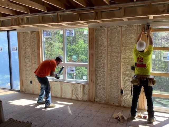 Two construction workers installing insulation in a new building, one hammering and the other holding a tool.