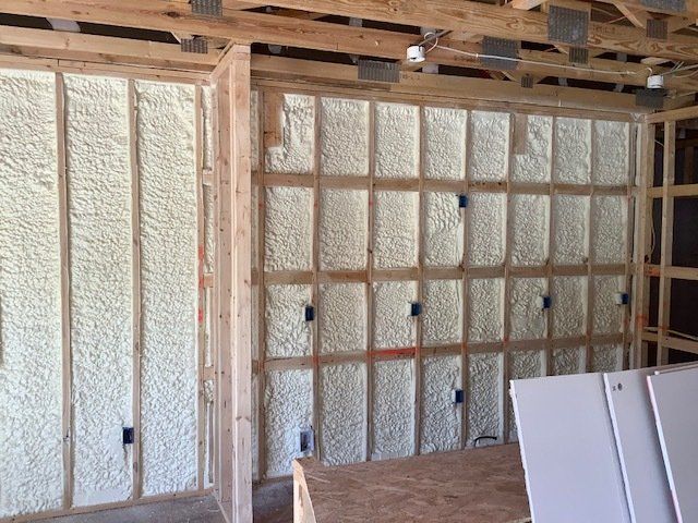 Interior walls of a building under construction, insulated with spray foam. Wooden framing is visible.