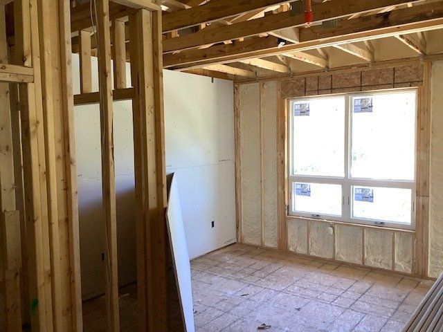 Interior view of a room under construction with exposed wooden framing and foam insulation around a window.
