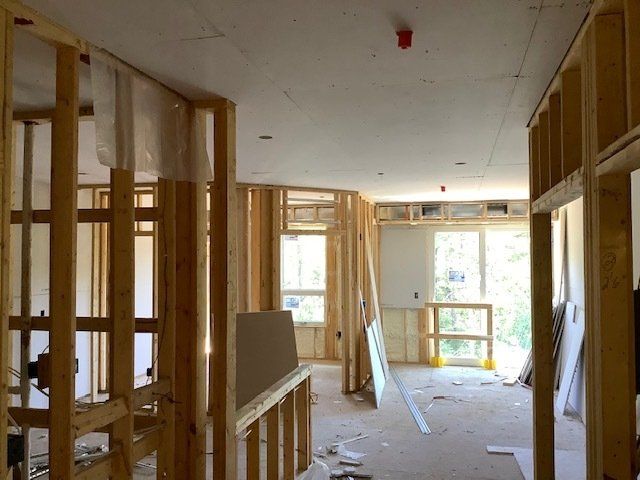 Interior of a house under construction. Wooden framing, drywall, and windows are visible.