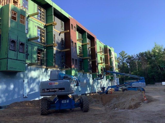 Building under construction with several blue lift machines. Green siding and exposed framing visible.