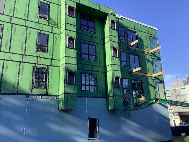 Building under construction, green sheathing, windows installed. Wooden supports, aerial lift.