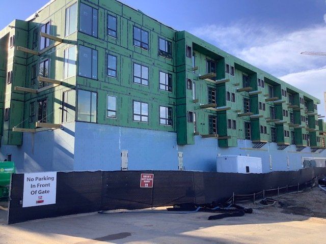 Building under construction, green sheathing, blue foundation, windows, black fencing.