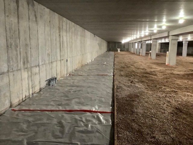 Concrete basement with plastic sheeting, gravel, and supporting pillars.