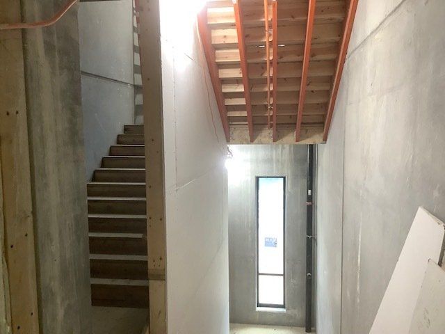 Stairwell under construction with wooden stairs, concrete walls, and window.