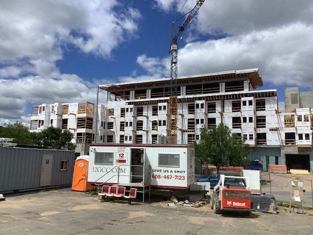Construction site with multi-story building frame, crane, and portable offices. Blue sky.