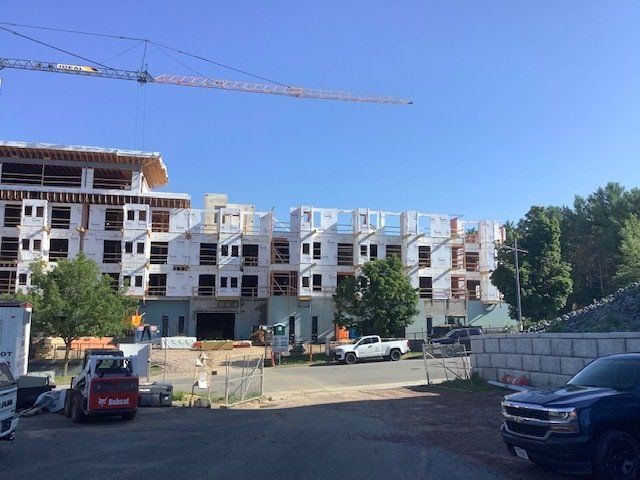 Construction site: multi-story building frames, crane, workers, clear sky.